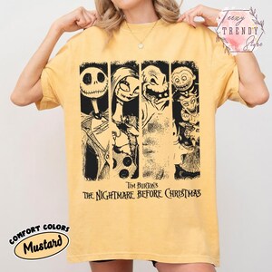 May include: A mustard yellow short-sleeve t-shirt featuring a black graphic print of characters from Tim Burton's The Nightmare Before Christmas. The design includes four vertical panels showing Jack Skellington, Sally, Oogie Boogie, and Lock, Shock, and Barrel.