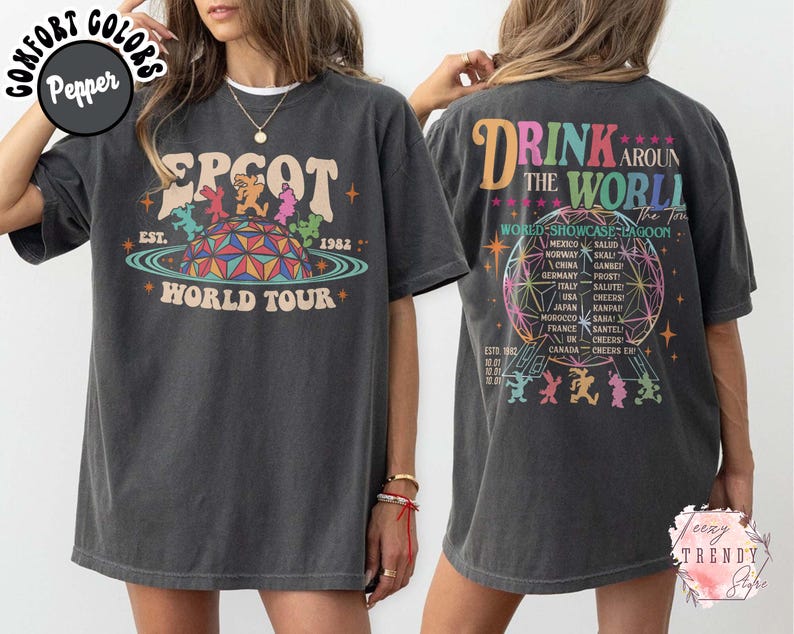 May include: Dark gray t-shirt featuring a colorful graphic of EPCOT World Tour with the text "EPCOT WORLD TOUR" and "EST. 1982". The back of the shirt has the text "DRINK AROUND THE WORLD" and a list of countries.
