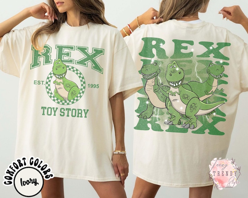 May include: Ivory-colored t-shirt featuring a green graphic of the character Rex from Toy Story. The front design includes the word "REX" above a cartoon dinosaur in a circle, with "EST. 1995" and "TOY STORY" below. The back has a larger Rex graphic.