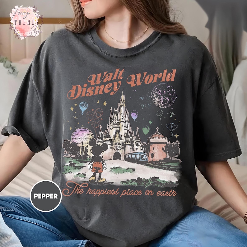 May include: Dark gray t-shirt featuring a colorful graphic of Walt Disney World. The design includes the castle, Mickey Mouse, and the text "Walt Disney World" and "The happiest place on earth".