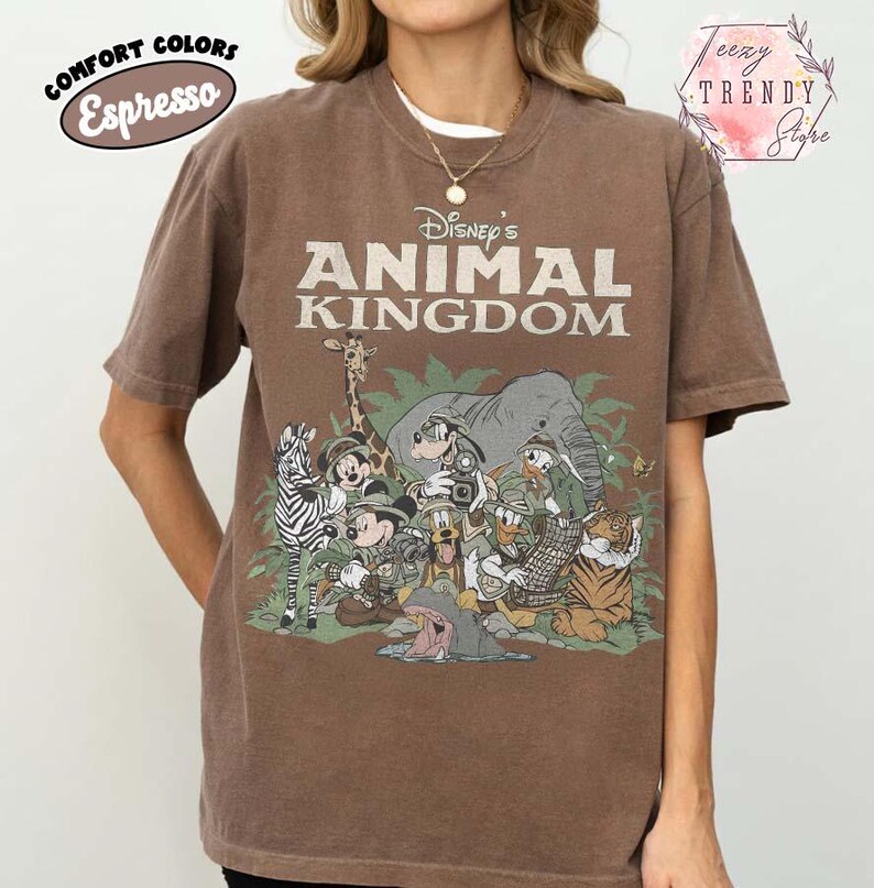 May include: Brown t-shirt with a graphic of Disney's Animal Kingdom characters, such as Mickey Mouse and Donald Duck. The words "Disney's Animal Kingdom" are printed on the front. The shirt is a comfort colors espresso.
