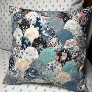 May include: Square decorative pillow with a patchwork design. The pillow features a variety of fabrics in shades of blue, cream, and gray, arranged in a circular pattern. Some circles have floral and bird motifs.