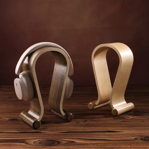 Puede incluir: Dos soportes para auriculares de madera, uno con un acabado marr&oacute;n claro y el otro con un acabado marr&oacute;n oscuro. Ambos soportes tienen forma de auricular y un dise&ntilde;o curvo.