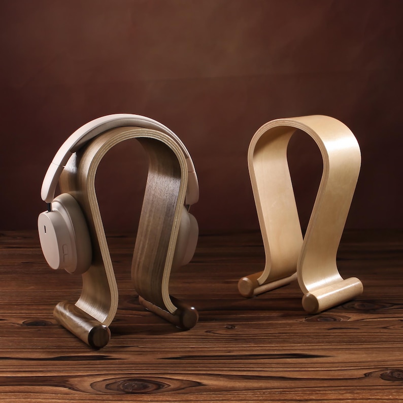 Puede incluir: Dos soportes para auriculares de madera, uno con un acabado marr&oacute;n claro y el otro con un acabado marr&oacute;n oscuro. Ambos soportes tienen forma de auricular y un dise&ntilde;o curvo.