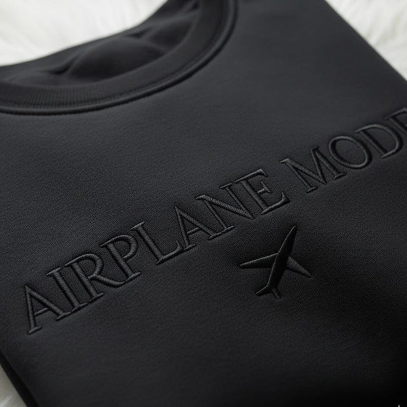 Puede incluir: Sudadera negra de cuello redondo con la inscripci&oacute;n "AIRPLANE MODE" bordada en hilo negro a juego en el pecho. Un peque&ntilde;o gr&aacute;fico de avi&oacute;n est&aacute; bordado debajo del texto. La sudadera est&aacute; hecha de una tela suave y texturizada.