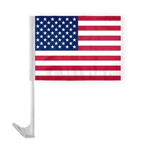 May include: A small American flag, featuring red and white stripes and a blue field with white stars, is mounted on a white plastic car window clip. The flag is designed for display on a vehicle.