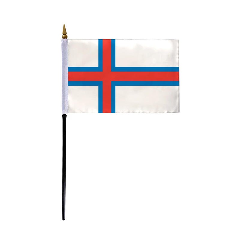 May include: A small desk flag of the Faroe Islands. The flag is white with a red cross outlined in blue.