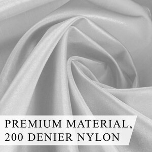May include: Close-up of white fabric with soft folds and a silky sheen. The text "PREMIUM MATERIAL, 200 DENIER NYLON" is displayed across the bottom. The fabric appears to be lightweight and flowing.