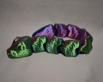 May include: A multi-colored, segmented bracelet with a textured surface. The bracelet features a gradient of colors, including green, purple, and blue. The bracelet is arranged in a circular shape, suggesting it is designed to be worn.