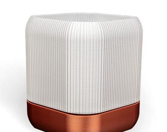 Puede incluir: Una lámpara de cerámica blanca con una base de cobre. La lámpara tiene un diseño acanalado y una forma cuadrada.