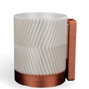 May include: A white ceramic cup with a copper-coloured base and a copper-coloured wall mount. The cup has a textured, chevron-like pattern.