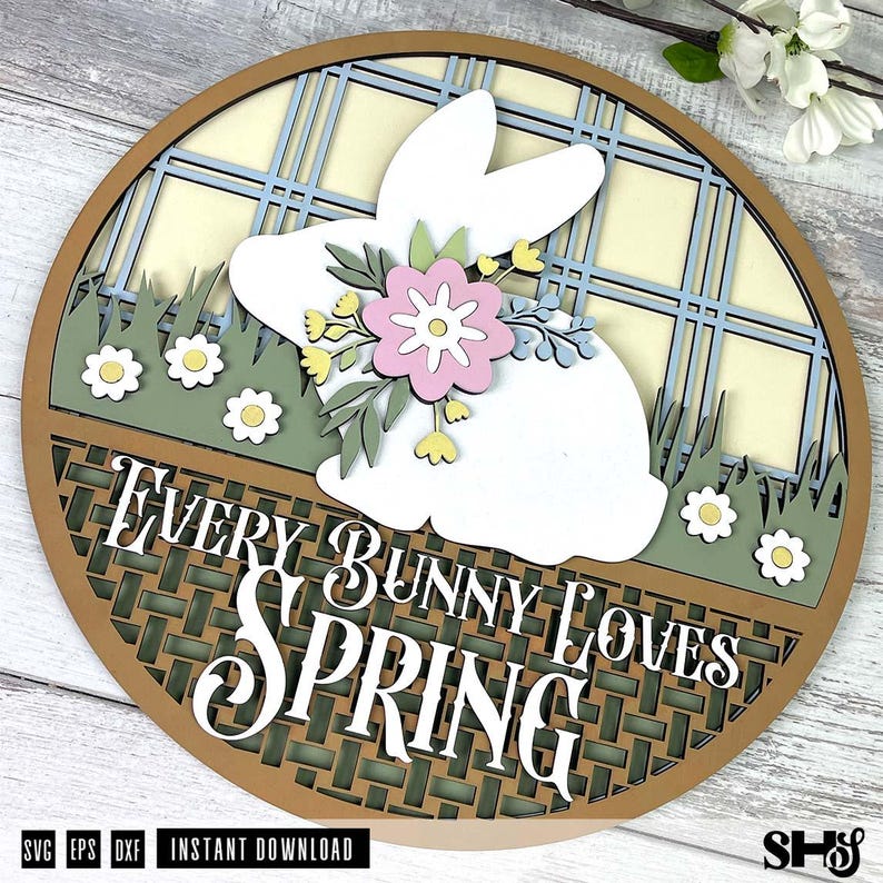 Pode incluir: Uma placa circular de madeira com a silhueta de um coelho branco adornada com uma flor rosa e detalhes amarelos. O fundo apresenta um padr&atilde;o xadrez azul claro e creme, relva verde com margaridas brancas e o texto EVERY BUNNY LOVES SPRING.
