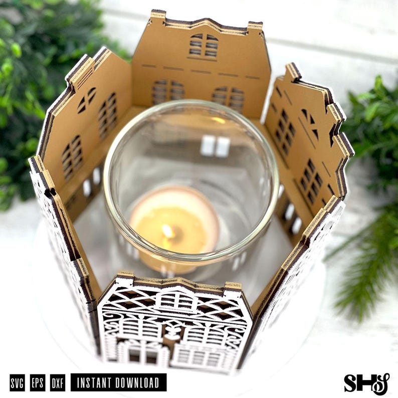 May include: A laser-cut wooden candle holder featuring a miniature house facade design surrounding a clear glass cylinder. A single lit tea light candle sits inside the glass. The wooden structure has intricate window and door cutouts.