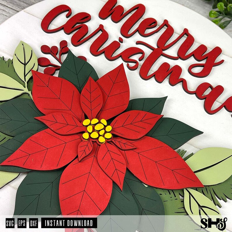 K&ouml;nnte beinhalten: Ein rundes wei&szlig;es Holzschild mit dem roten Schriftzug Merry Christmas in Schreibschrift. Das Schild ist mit geschichteten, ausgeschnittenen Weihnachtssternen in Rot und Dunkelgr&uuml;n sowie hellgr&uuml;nen Bl&auml;ttern und kleinen roten Beeren verziert.