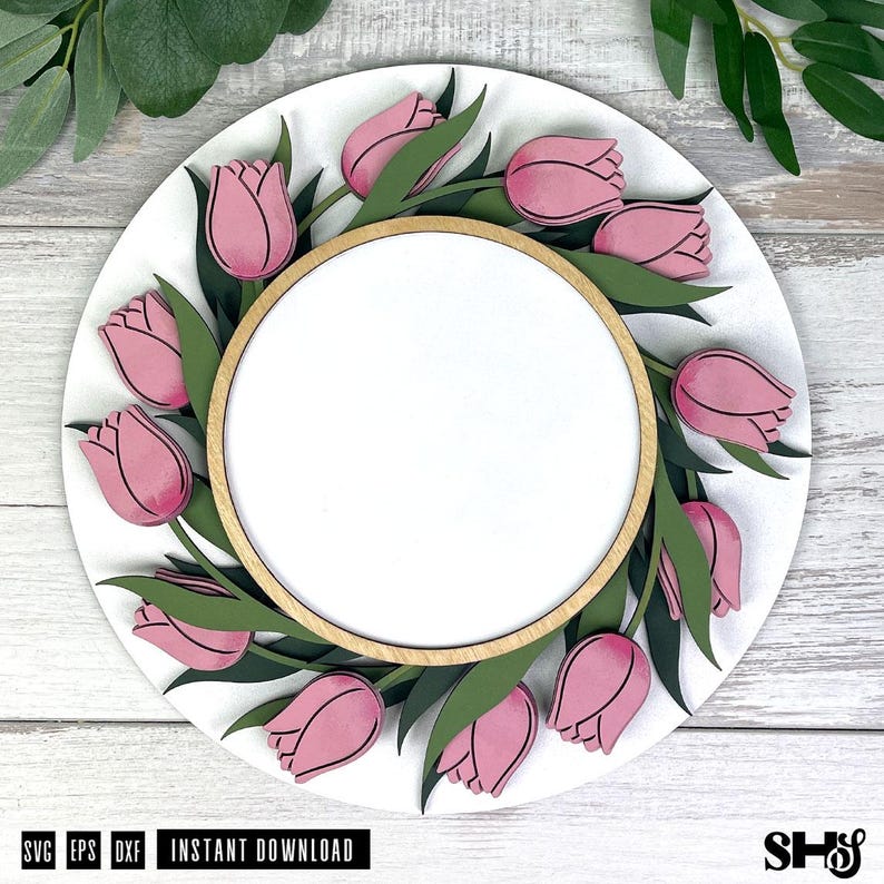 May include: A circular wooden sign featuring a layered design of pink tulips and dark green leaves arranged in a wreath pattern around a central blank white circle. The sign has a natural light wood border and a smooth white background finish.