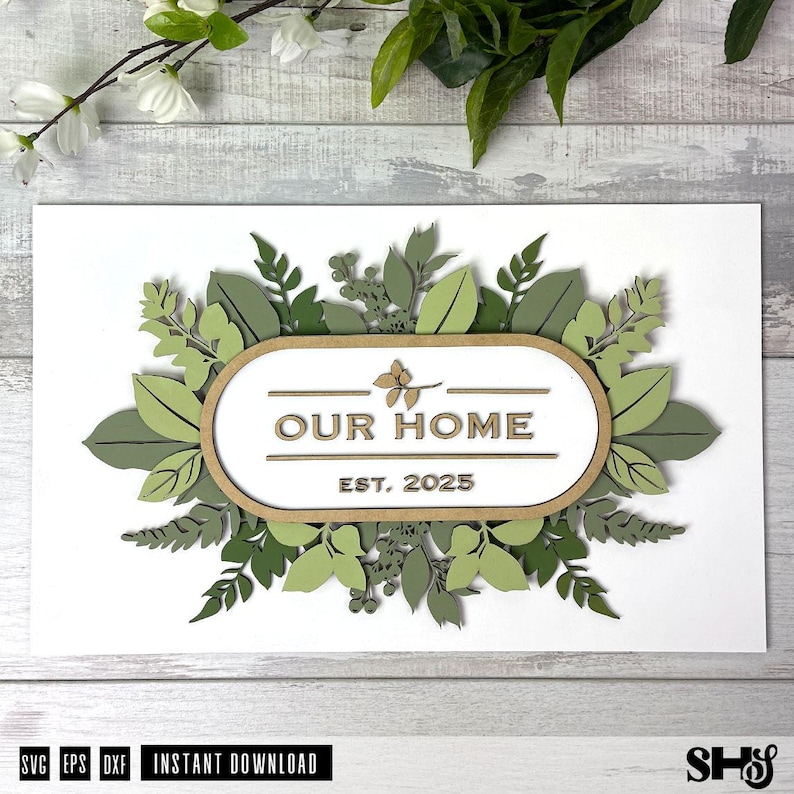 May include: A white sign with a brown wooden frame and green leafy foliage around the edges. The sign says "Our Home Est. 2025".