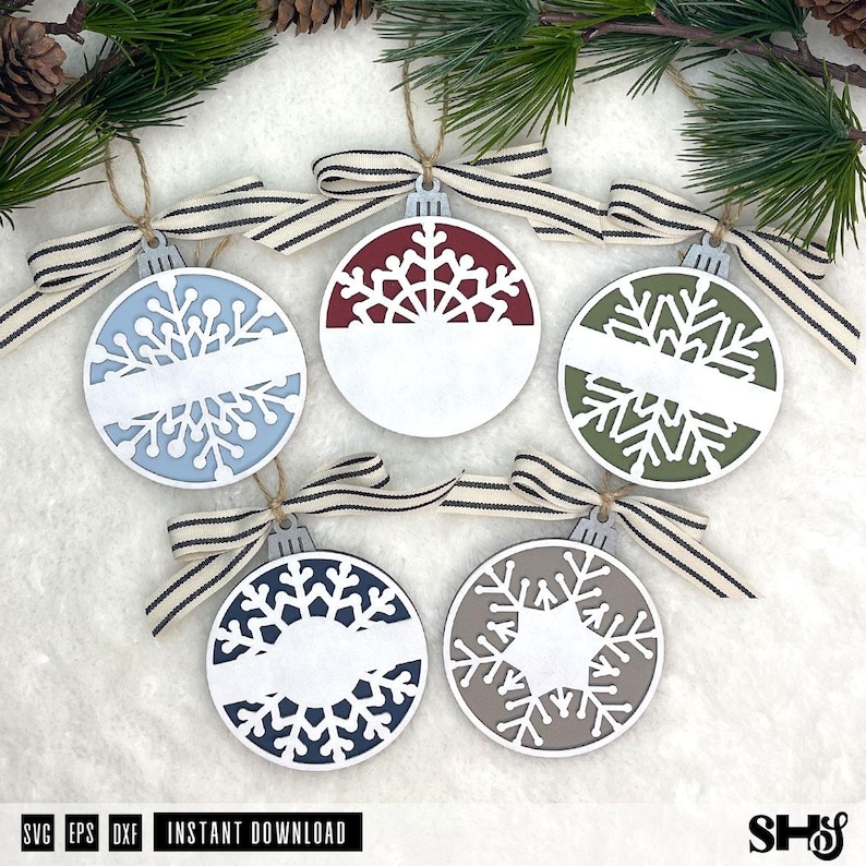 May include: Five circular wooden Christmas ornaments featuring intricate snowflake cutouts and a horizontal blank space for personalisation. Each ornament is topped with a silver-toned cap and a beige and black striped fabric ribbon bow.