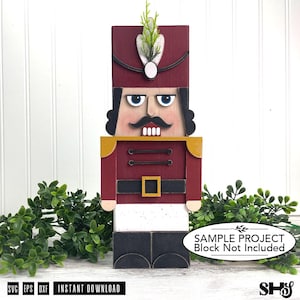 May include: A wooden nutcracker figure featuring a tall maroon hat with a white feather accent, a maroon jacket with gold shoulder details, a black belt with a gold buckle, white trousers, and black boots, with a mustache and blue eyes.