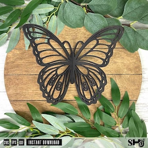 May include: A dark brown, laser-cut butterfly silhouette featuring intricate, symmetrical wing patterns with open-work detailing. The butterfly is centered on a circular, light brown wooden plaque with horizontal grain lines and visible wood texture.