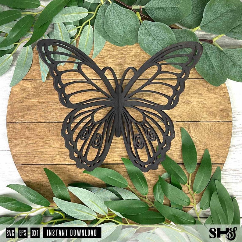 May include: A dark brown, laser-cut butterfly silhouette featuring intricate, symmetrical wing patterns with open-work detailing. The butterfly is centered on a circular, light brown wooden plaque with horizontal grain lines and visible wood texture.