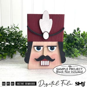 May include: A wooden nutcracker block featuring a deep red hat with a white feather, black hair, blue eyes, a tan nose, a black mustache, and white teeth. The block includes text that reads: SAMPLE PROJECT Block Not Included.