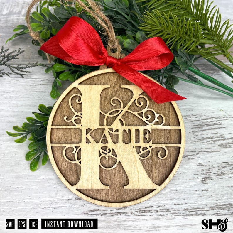 Op de afbeelding: Een ronde houten ornament met een grote uitgesneden letter K met de naam Katie in het midden verwerkt. Het ontwerp bevat decoratieve krullen en een felrood satijnen lint dat aan de bovenkant tot een strik is gebonden.