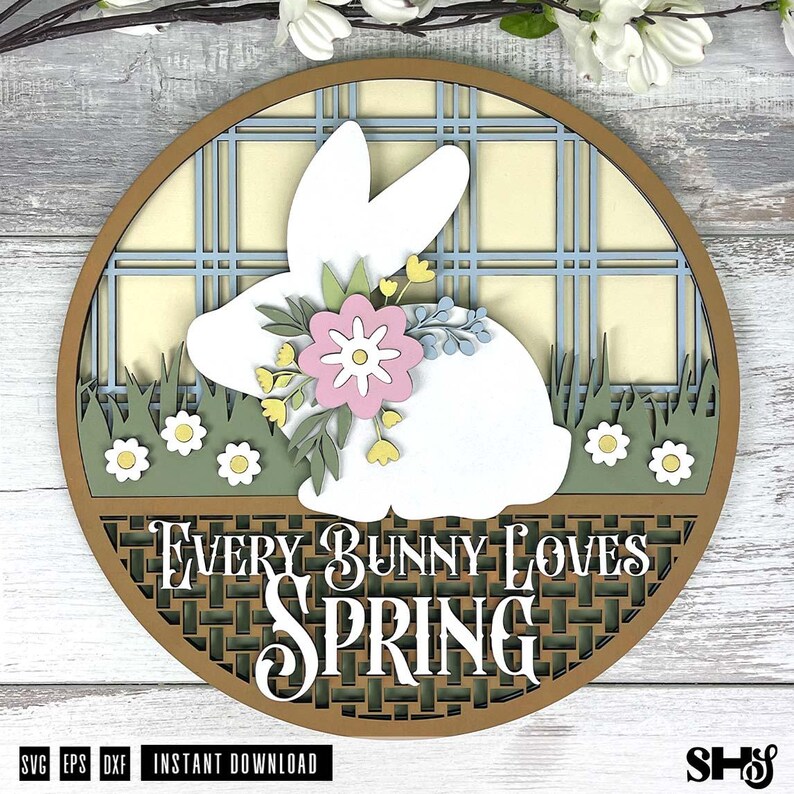 Pode incluir: Uma placa circular de madeira em camadas com a silhueta de um coelho branco adornado com uma flor rosa e folhas verdes. O fundo apresenta um padr&atilde;o xadrez azul claro e grama verde com flores brancas. O texto diz Every Bunny Loves Spring.