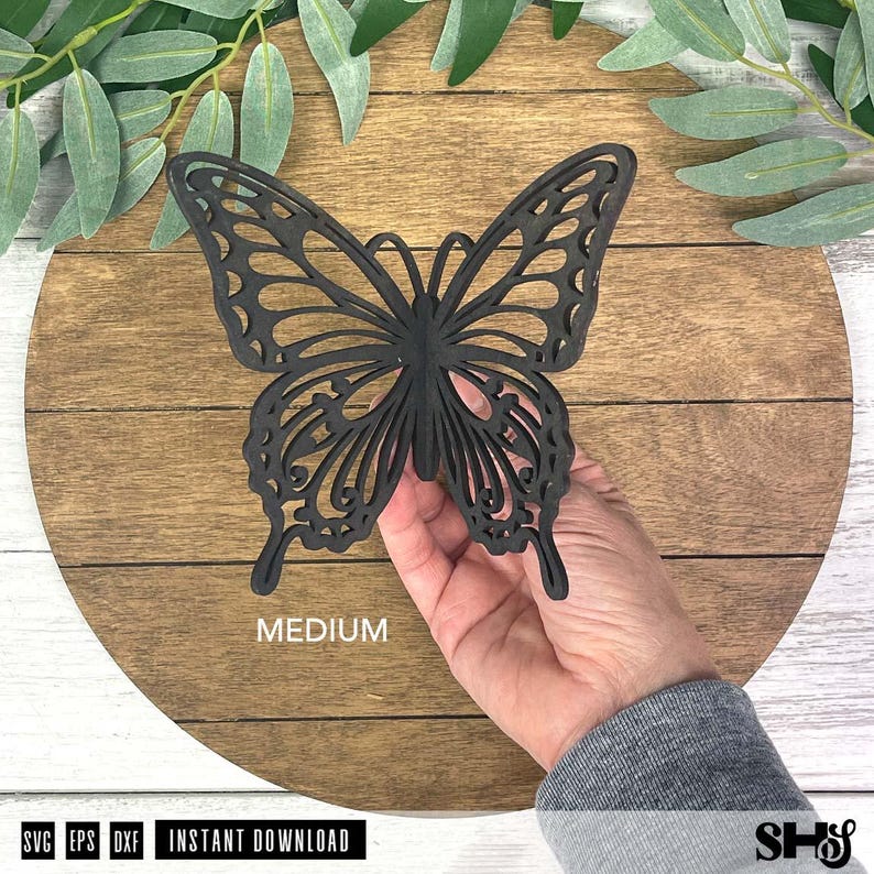 May include: A black laser-cut butterfly silhouette with intricate wing patterns. The butterfly is held in place and features the word MEDIUM printed in white text below it. The design is flat and features a detailed, symmetrical cutout structure.