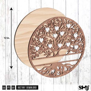 May include: A circular wooden wall art piece featuring a laser-cut tree design with intricate branches and roots. The design includes several small white heart-shaped cutouts integrated into the foliage. A measurement arrow indicates a 12 in. diameter.