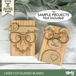 May include: Two laser-cut wooden glasses blanks. One is a scarecrow design with a flower and a smiling face. The other is a bear design with a heart. The text on the image says "BLANKS CUT FOR YOU" and "SAMPLE PROJECTS Not Included". The bottom text says "LASER CUT GLASSES BLANKS".
