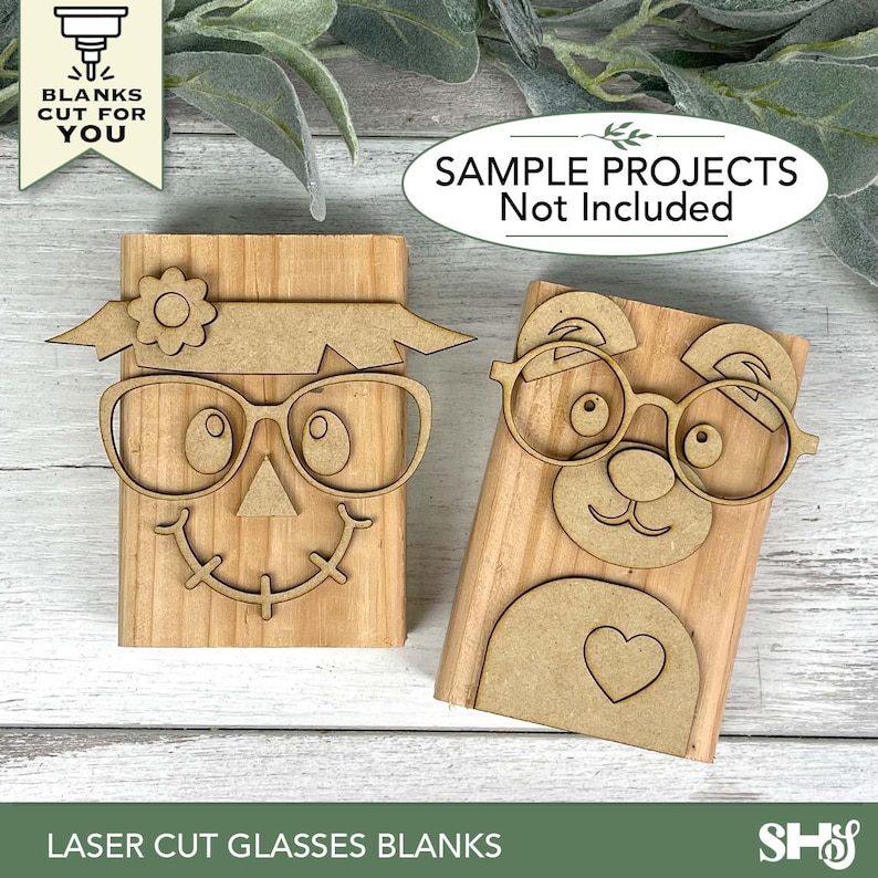 May include: Two laser-cut wooden glasses blanks. One is a scarecrow design with a flower and a smiling face. The other is a bear design with a heart. The text on the image says "BLANKS CUT FOR YOU" and "SAMPLE PROJECTS Not Included". The bottom text says "LASER CUT GLASSES BLANKS".