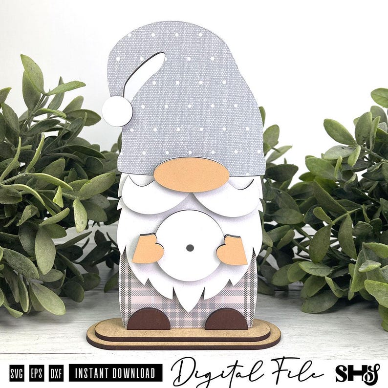 May include: A layered wooden gnome cutout featuring a light grey hat with white polka dots, a peach-coloured nose, a white beard, and a plaid patterned body. The gnome stands on a flat oval base and holds a circular white element with a small dot.
