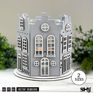 May include: A gray laser-cut wooden candle holder shaped like a miniature house with multiple windows and doors. The structure features a circular window at the top and a central arched doorway. A circular base supports the house-shaped frame.