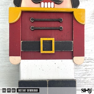 May include: A wooden nutcracker cutout featuring a red jacket with yellow shoulder accents, a black belt with a yellow square buckle, and white trousers. The design includes two horizontal black bars on the chest and black boots. Text reads SVG EPS DXF INSTANT DOWNLOAD.