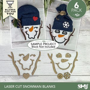 May include: A set of laser-cut wooden snowman face components including branch arms, carrot noses, eyes, mouths, hearts, buttons, and snowflake shapes. The kit includes pieces to create two distinct snowman designs, featuring dark blue knit hats.