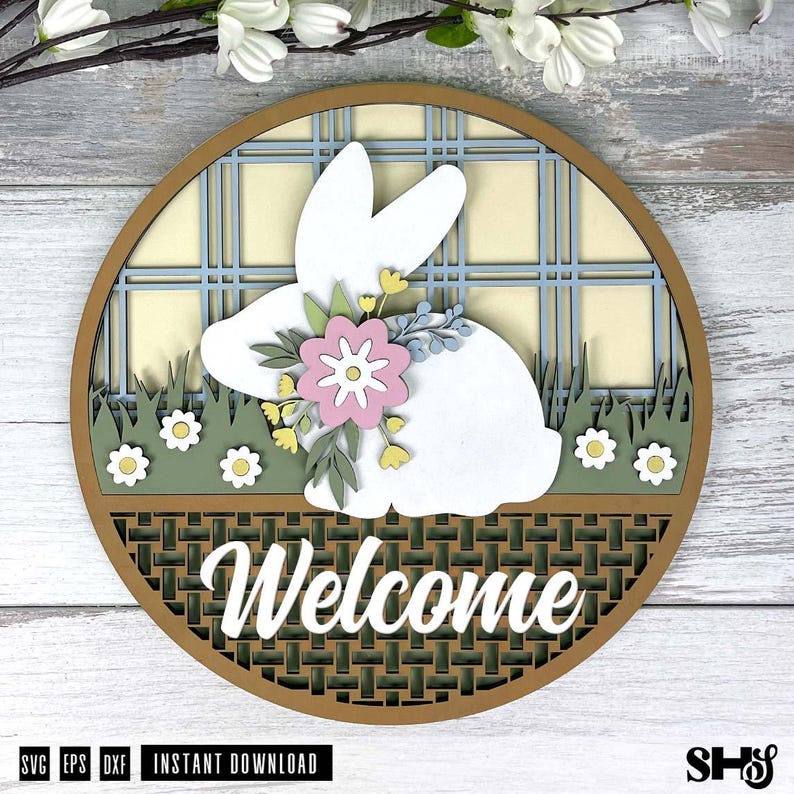 Pode incluir: Uma placa circular de madeira em camadas com a silhueta de um coelho branco adornado com uma flor rosa e folhas verdes. O fundo apresenta um padr&atilde;o xadrez azul e creme sobre uma &aacute;rea de relva verde com pequenas flores brancas e base tran&ccedil;ada.
