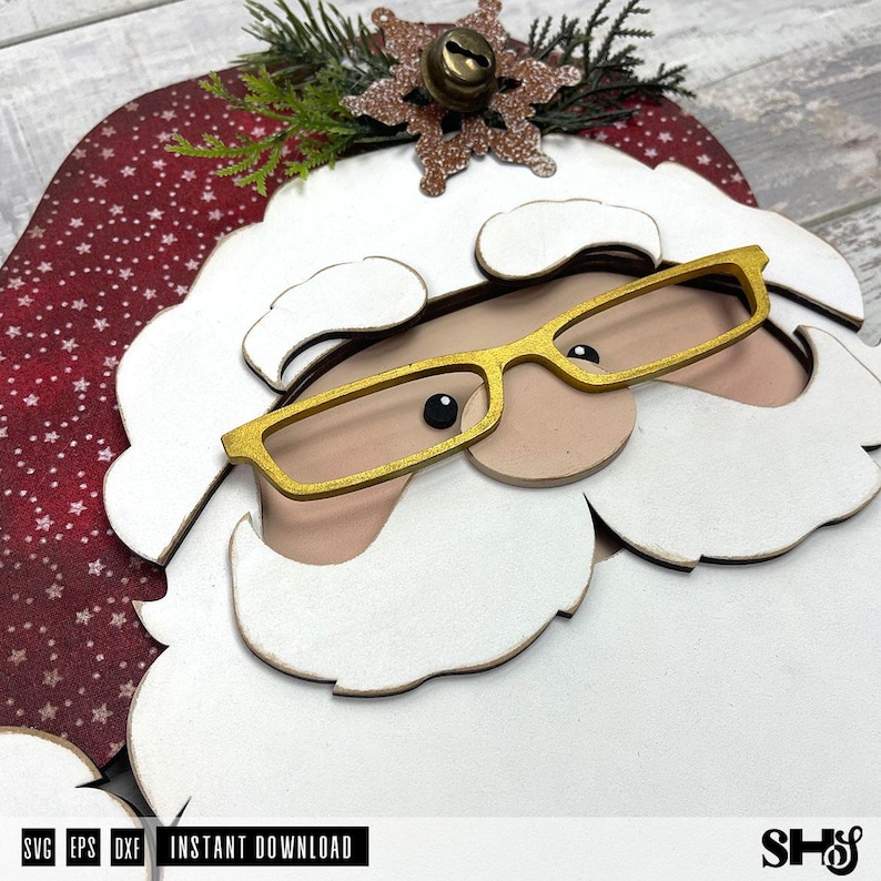 K&ouml;nnte beinhalten: Eine mehrschichtige Holzdekoration in Form eines Weihnachtsmanns mit roter M&uuml;tze mit wei&szlig;en Sternen, wei&szlig;em Bart und Schnurrbart sowie einer goldfarbenen Brille. Oben befindet sich eine glitzernde braune Schneeflocke mit kleiner Metallglocke und Tannennadeln.
