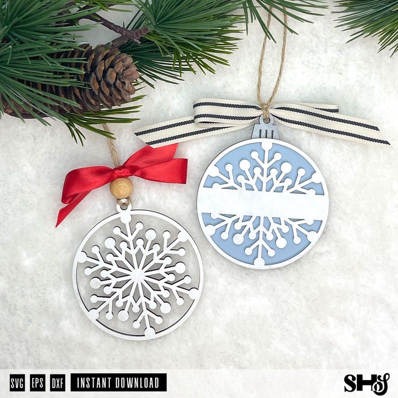 May include: Two circular snowflake ornaments. One is white with a red ribbon and wooden bead. The other has a light blue background, a white snowflake cutout, a horizontal white bar for personalisation, and a striped beige and black ribbon.