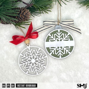 May include: Two circular snowflake ornaments. One is white with a red ribbon and wooden bead. The other is olive green with a white centre stripe and a black and white striped ribbon. Both feature intricate snowflake cutouts and twine loops.
