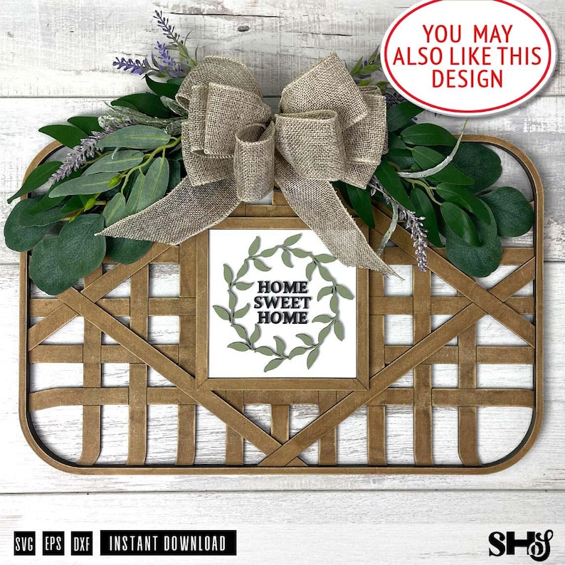 May include: A wooden sign with a woven frame and a burlap bow. The sign has a white background with a green wreath and the text "Home Sweet Home" in black.