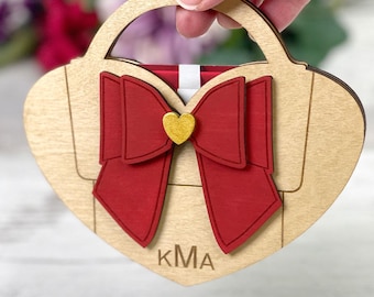May include: Wooden heart-shaped purse with a red bow and a gold heart-shaped accent. The purse has a handle and the initials "KmA" are visible. The bottom of the image includes the text "SVG EPS DXF INSTANT DOWNLOAD".