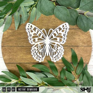 May include: A white laser-cut butterfly silhouette featuring intricate geometric wing patterns and symmetrical cutouts. The butterfly is centered and displays a clean, flat design with sharp edges, showcasing a detailed openwork structure.