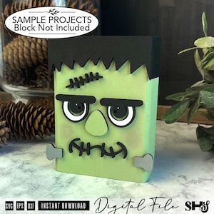 May include: A light green rectangular wooden block decorated as a monster character with black hair, thick black eyebrows, a stitched forehead scar, a central nose, and a stitched mouth. Two grey bolts are attached to the sides of the block.