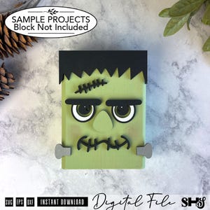 May include: A light green rectangular wooden block decorated as a monster face with black hair, thick black eyebrows, a central nose, and a stitched mouth. The design includes two grey bolts on the sides and a black stitched scar on the forehead.