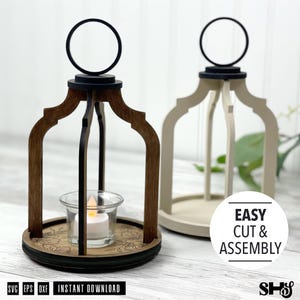 May include: Two decorative lantern frames made of wood, one dark brown and one cream, featuring arched supports and a circular top handle. A clear glass tea light holder with a small white LED candle sits inside the dark brown lantern base.