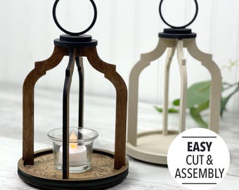 May include: Two wooden candle lanterns, one brown and one white, with black metal handles. The lanterns are designed for tea lights and have a floral design on the base. The text "EASY CUT & ASSEMBLY" is visible in the image.