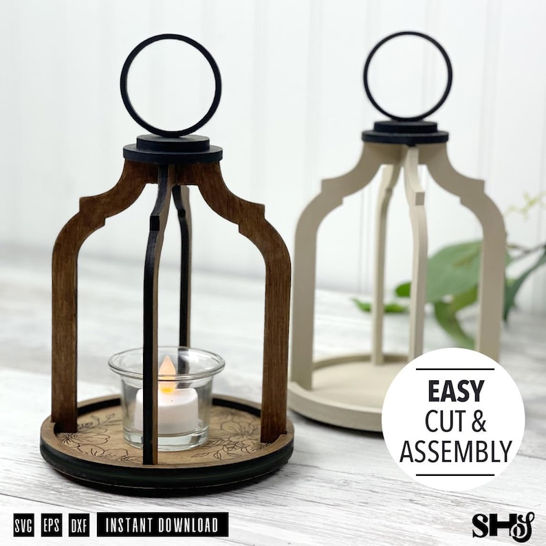 May include: Two decorative lantern frames made of wood, one dark brown and one cream, featuring arched supports and a circular top handle. A clear glass tea light holder with a small white LED candle sits inside the dark brown lantern base.