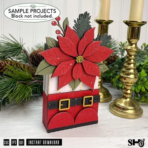 May include: A decorative wooden craft project featuring a red poinsettia flower with green leaves and pine sprigs atop a base designed to look like red boots with a black belt and gold buckles. The text reads SAMPLE PROJECTS Block not included.