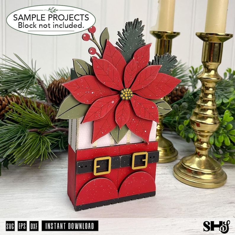 May include: A decorative wooden craft project featuring a red poinsettia flower with green leaves and pine sprigs atop a base designed to look like red boots with a black belt and gold buckles. The text reads SAMPLE PROJECTS Block not included.