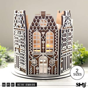 May include: A brown and white laser-cut wooden house-shaped candle holder featuring intricate architectural details, arched windows, and heart-shaped cutouts. The structure is composed of multiple panels with a scalloped roof design and a circular base.